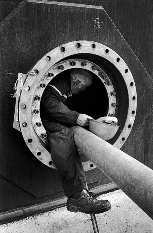 Gestes du travail | Photographie en N/B d'un homme qui rentre dans une cuve de pétrole vide